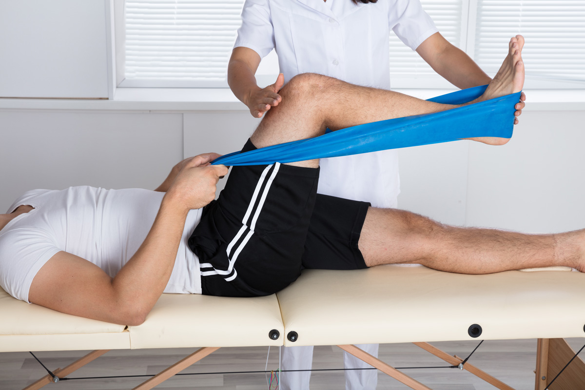 A person lying down stretching their leg with the help of a physical therapist in El Paso.