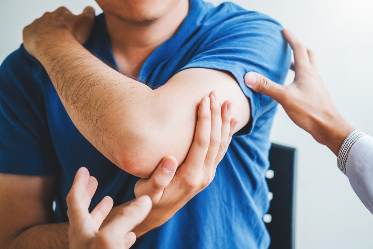 A person in a blue t-shirt stretching their arm with the assistance of a physical therapist in El Paso.