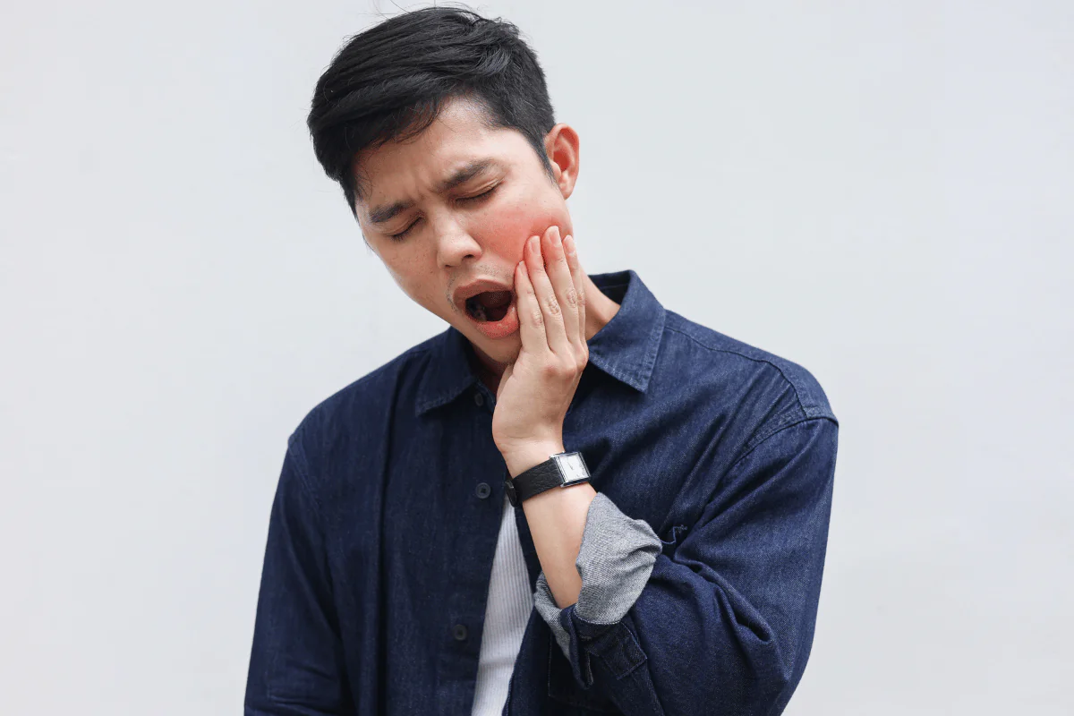 A young man holding his jaw in pain.